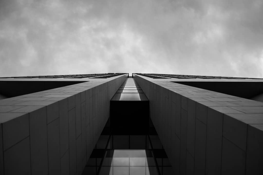 Looking up the symmetrical face of a modern tower into the sky, in black and white